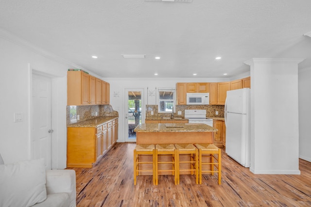 kitchen with a breakfast bar area, crown molding, a center island, white appliances, and light hardwood / wood-style floors