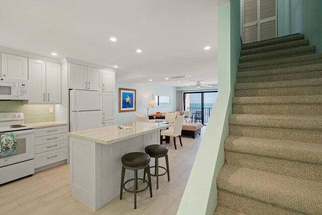 kitchen with tasteful backsplash, white cabinets, a kitchen bar, a center island, and white appliances