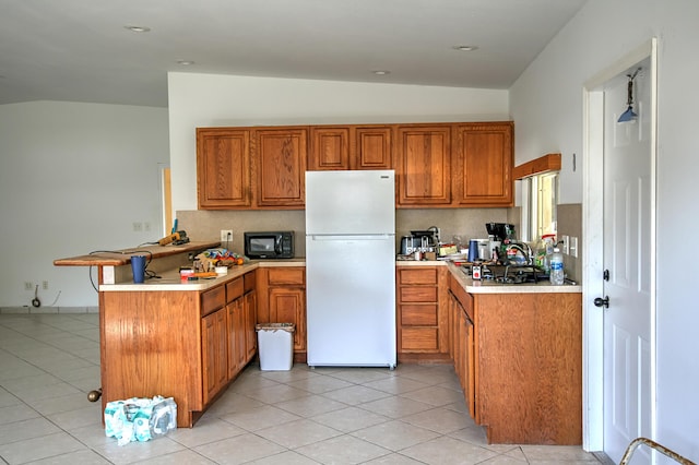 kitchen with light tile patterned floors, backsplash, kitchen peninsula, and white fridge