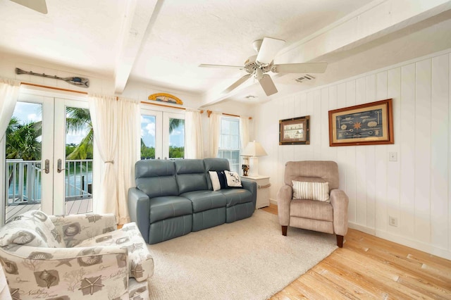 living room with beam ceiling, ceiling fan, light hardwood / wood-style floors, and french doors