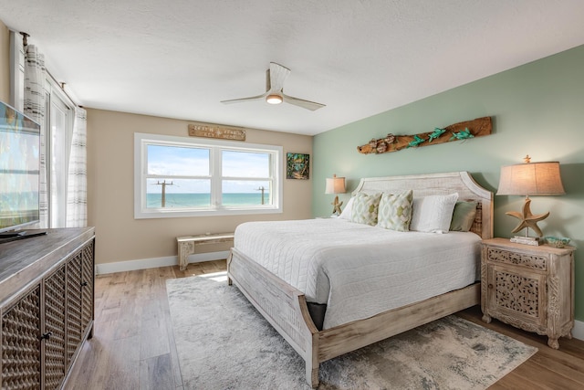 bedroom featuring light hardwood / wood-style flooring, ceiling fan, and a water view