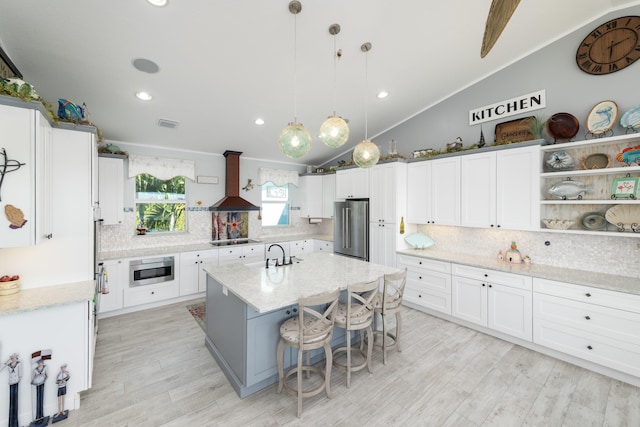 kitchen featuring wall chimney range hood, a breakfast bar, hanging light fixtures, a center island with sink, and high end refrigerator