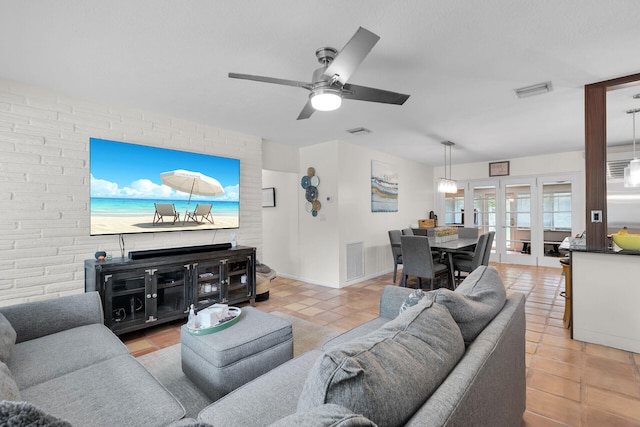 living room featuring light tile patterned floors, french doors, ceiling fan, and brick wall