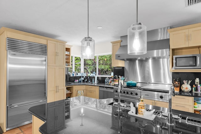 kitchen with wall chimney exhaust hood, light brown cabinetry, high end appliances, hanging light fixtures, and dark stone counters