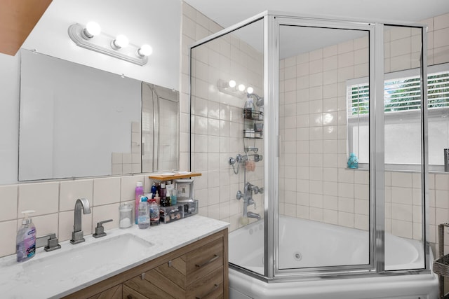 bathroom featuring vanity, combined bath / shower with glass door, tile walls, and backsplash