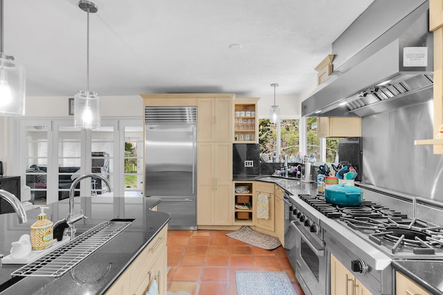 kitchen featuring premium appliances, light tile patterned floors, hanging light fixtures, and wall chimney exhaust hood