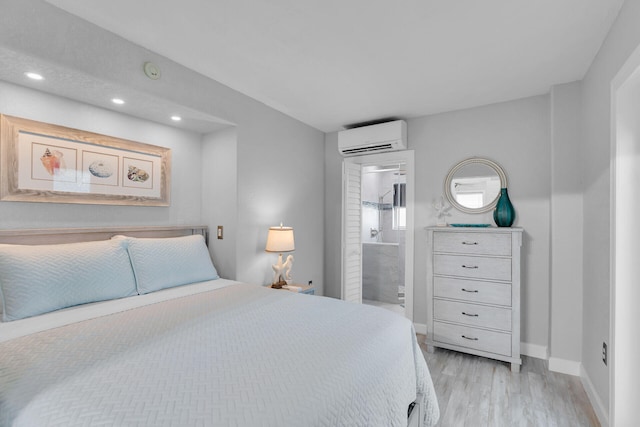 bedroom with a wall unit AC, light wood-style floors, recessed lighting, baseboards, and ensuite bath