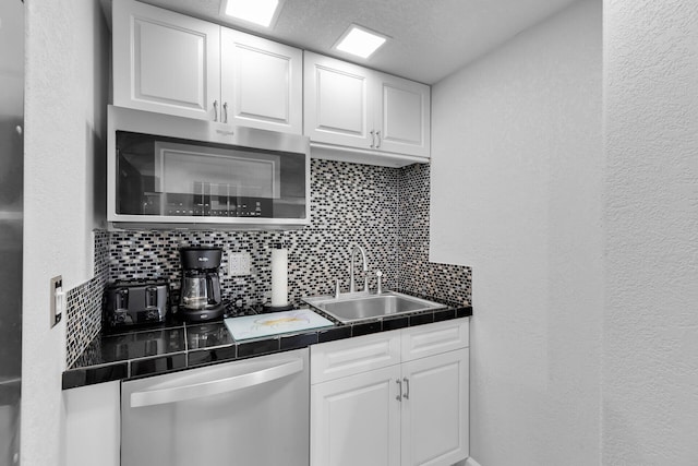 kitchen featuring appliances with stainless steel finishes, a sink, backsplash, white cabinetry, and a textured wall