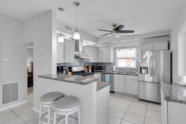 kitchen featuring appliances with stainless steel finishes, wall chimney exhaust hood, a peninsula, ceiling fan, and a sink