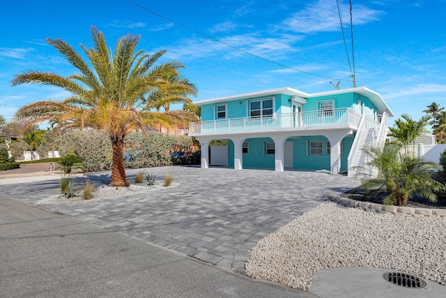 beach home featuring decorative driveway, stucco siding, a carport, a balcony, and a porch