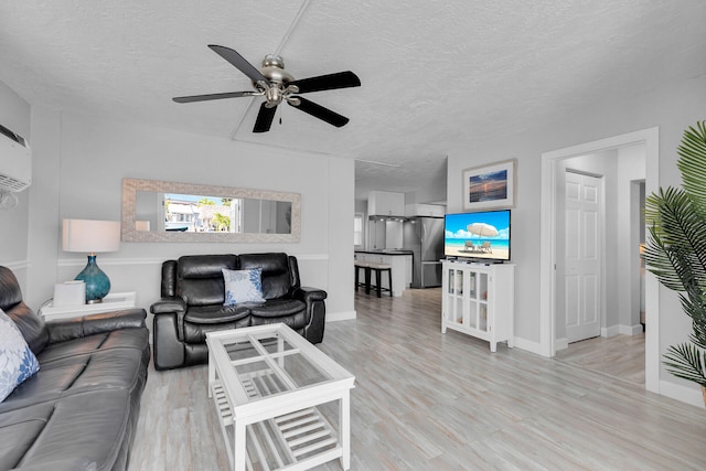 living area featuring a textured ceiling, wood finished floors, ceiling fan, and baseboards