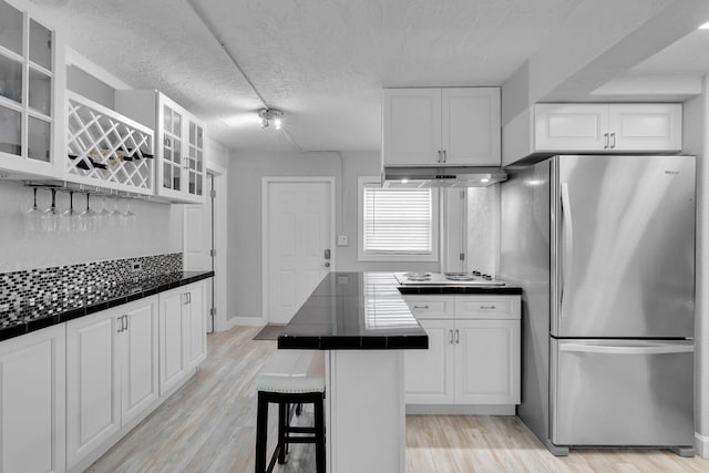 kitchen featuring freestanding refrigerator, tile countertops, white cabinetry, a kitchen breakfast bar, and a textured ceiling