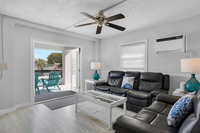 living room with a wall mounted AC, a ceiling fan, light wood-style floors, and a textured ceiling