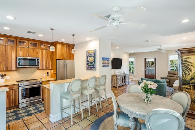 kitchen featuring stainless steel appliances, light countertops, hanging light fixtures, glass insert cabinets, and open floor plan