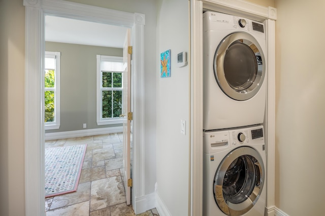 laundry room featuring stone tile flooring, baseboards, and stacked washing maching and dryer