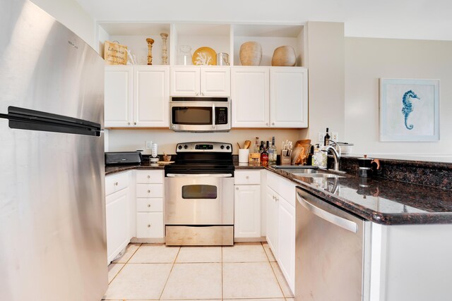 kitchen featuring light tile patterned flooring, appliances with stainless steel finishes, white cabinetry, sink, and dark stone countertops