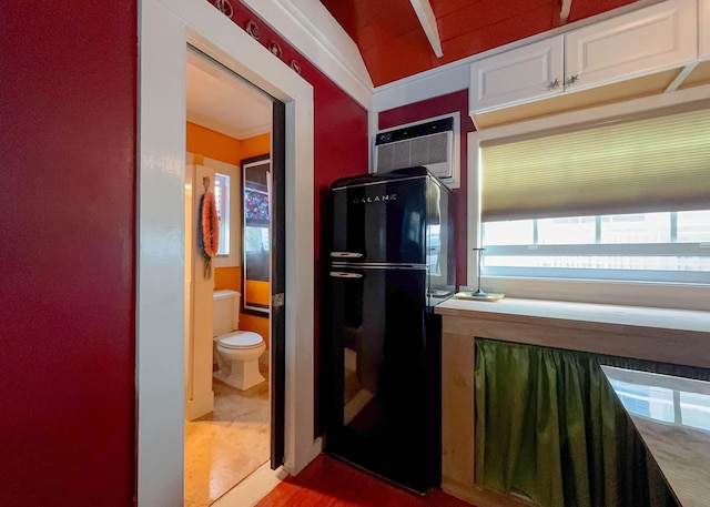 kitchen featuring black refrigerator, a wall mounted air conditioner, and white cabinets