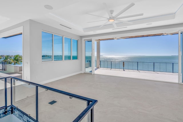 interior space featuring a raised ceiling, a water view, plenty of natural light, and ceiling fan