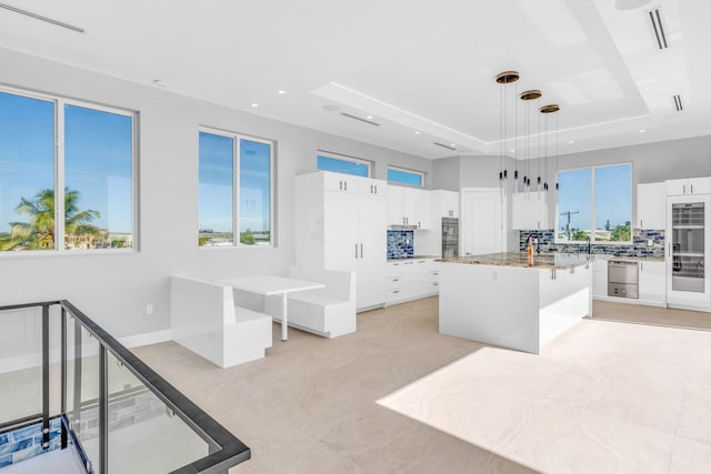 kitchen with pendant lighting, white cabinetry, a center island, a tray ceiling, and light stone countertops