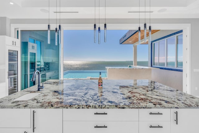 kitchen featuring pendant lighting, sink, white cabinetry, plenty of natural light, and a water view