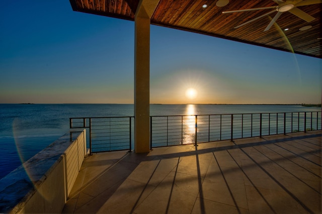 deck at dusk with a water view and ceiling fan