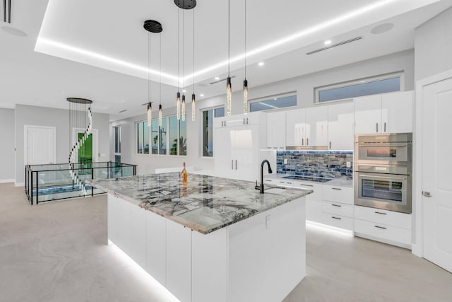 kitchen with sink, pendant lighting, stainless steel double oven, light stone countertops, and white cabinets