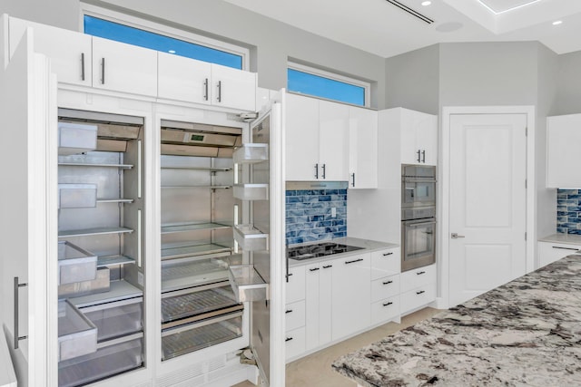 kitchen with light stone countertops, decorative backsplash, stainless steel appliances, and white cabinets