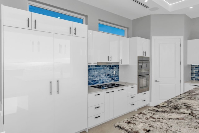 kitchen with black electric cooktop, white cabinetry, light stone counters, and backsplash