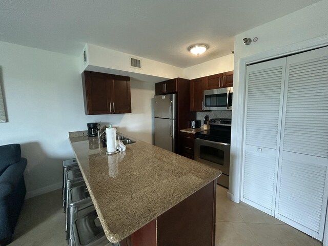 kitchen with appliances with stainless steel finishes, a breakfast bar, sink, light tile patterned floors, and kitchen peninsula