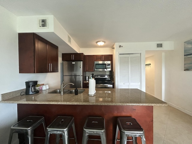 kitchen with appliances with stainless steel finishes, a breakfast bar, sink, light tile patterned floors, and kitchen peninsula