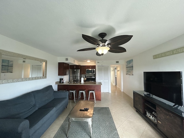 living room featuring light tile patterned flooring, ceiling fan, sink, and a textured ceiling