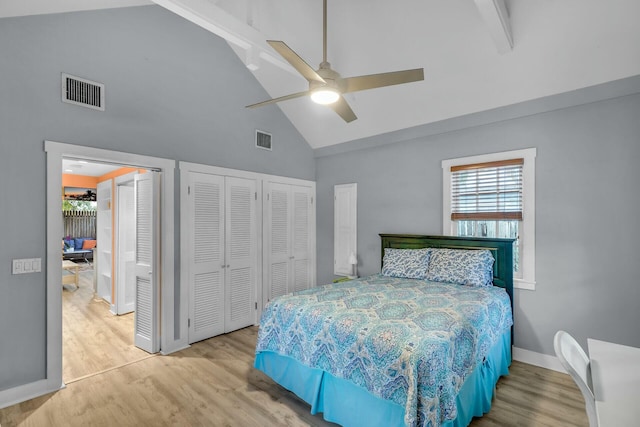 bedroom featuring multiple closets, visible vents, high vaulted ceiling, and wood finished floors