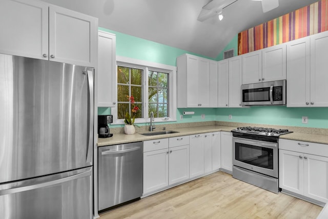 kitchen with lofted ceiling, stainless steel appliances, a sink, light countertops, and light wood-type flooring