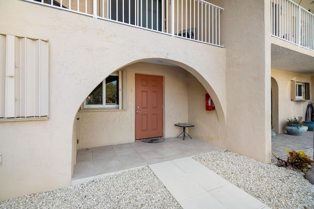 view of exterior entry featuring a patio area, a balcony, and stucco siding