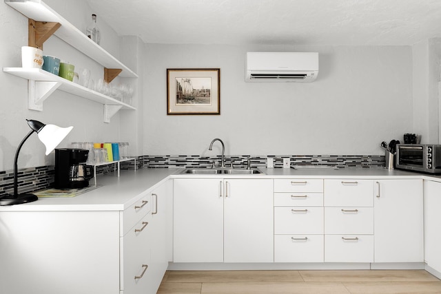 kitchen featuring sink, white cabinets, a wall unit AC, and light hardwood / wood-style flooring