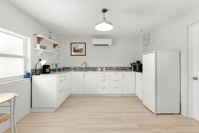 kitchen featuring decorative light fixtures, white cabinetry, white fridge, a wall unit AC, and light hardwood / wood-style flooring