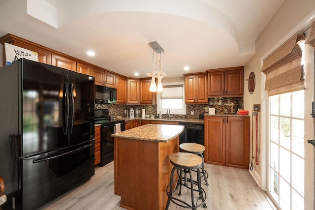 kitchen featuring a kitchen island, a sink, brown cabinets, decorative backsplash, and black appliances