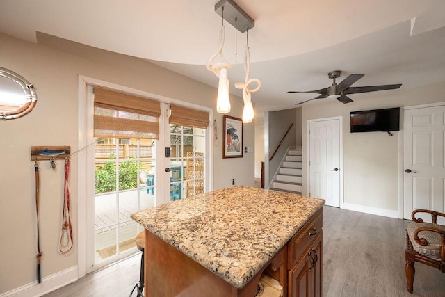 kitchen with light stone counters, light wood-style flooring, a kitchen island, baseboards, and brown cabinetry