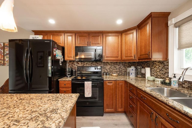 kitchen featuring backsplash, brown cabinetry, light wood-style floors, a sink, and black appliances