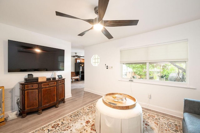 living area with a ceiling fan, light wood-type flooring, and baseboards