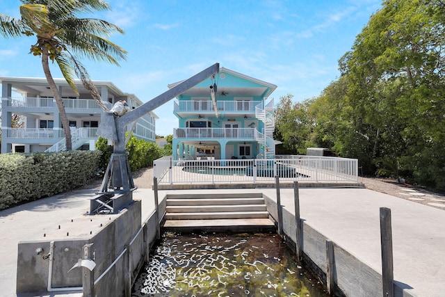 rear view of property with a balcony, ceiling fan, stairs, a patio area, and an outdoor pool