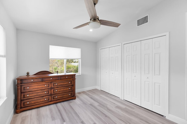 bedroom with multiple closets, vaulted ceiling, light wood-type flooring, baseboards, and ceiling fan