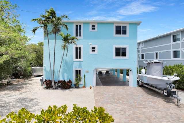 back of property featuring a carport, decorative driveway, central AC, and stucco siding