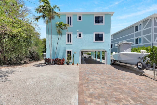 back of property with a carport, decorative driveway, and stucco siding