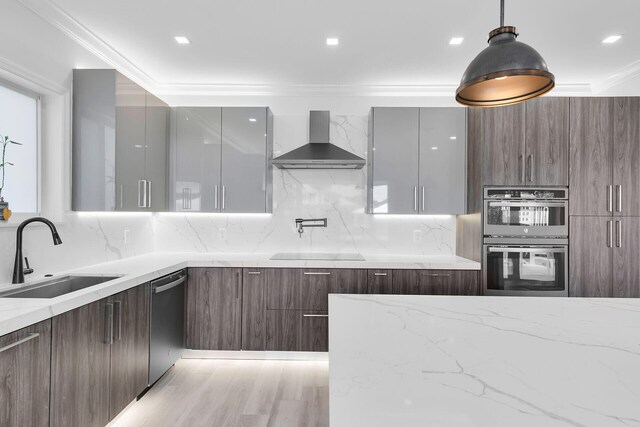 kitchen featuring modern cabinets, wall chimney range hood, appliances with stainless steel finishes, a sink, and ornamental molding