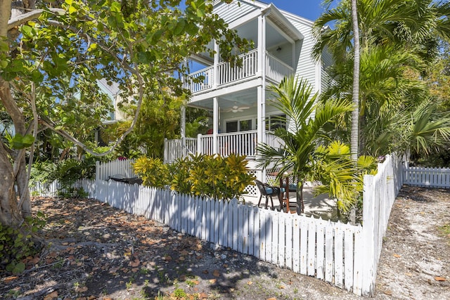 view of side of property featuring a porch, a balcony, a ceiling fan, and a fenced front yard