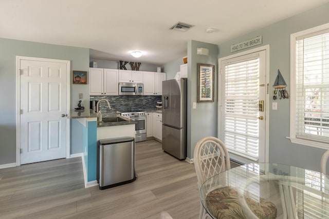 kitchen featuring tasteful backsplash, light wood-style flooring, white cabinets, stainless steel appliances, and a sink