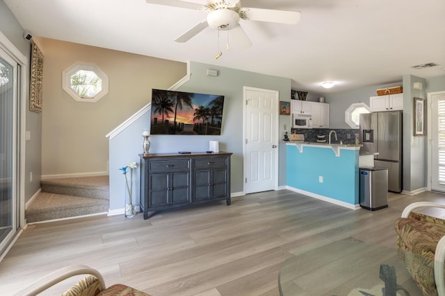 living room with visible vents, light wood-style flooring, a ceiling fan, and baseboards