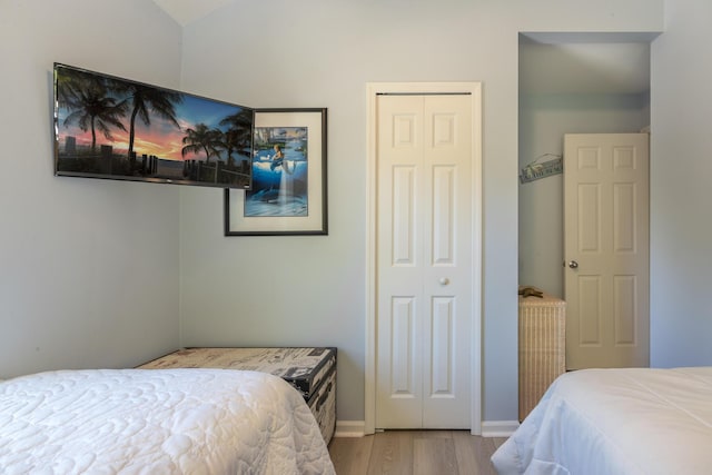 bedroom with vaulted ceiling, wood finished floors, a closet, and baseboards