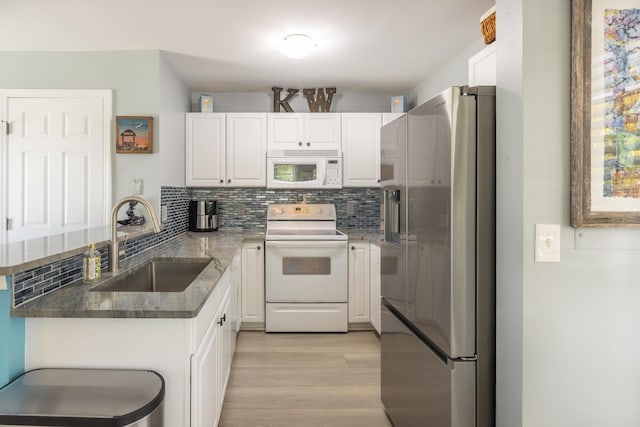 kitchen featuring a sink, tasteful backsplash, white cabinetry, white appliances, and a peninsula